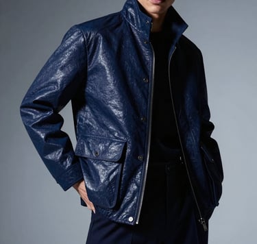 High-fashion editorial photography of a visionary artist in a North American / US studio. The subject wears a structured midnight blue jacket, standing in a powerful, confident pose. The lighting is dramatic and moody, with soft silver-blue highlights reflecting off the fabric. Immersive, sophisticated atmosphere.