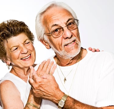 two elderly home care service users smiling, the elderly woman has hand laid upon elderly man.