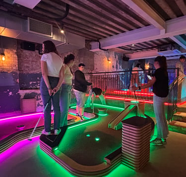Estudiantes jugando al minigolf en un local de ocio iluminado con luces de neón