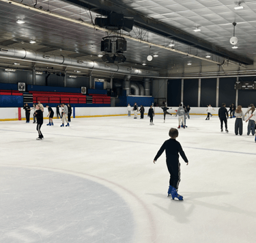 Un grupo de estudiantes patinando sobre hielo en una gran pista de hielo pública cubierta 