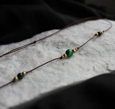 eine filigrane Kette mit grünen und goldenen Perlen liegt auf einem Stein