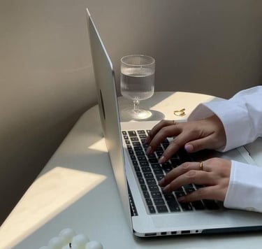 Hands typing on a laptop next to a glass of water in a minimal workspace.