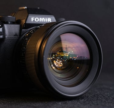 Close-up of a high-end camera lens reflecting the city lights of Istanbul at dusk. The background is a soft-focus dark slate black, with subtle metallic gold glimmers on the camera's body.