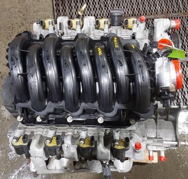 High-performance V8 car engine with black intake manifold and silver block in an auto repair shop.