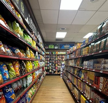 Aisle in Round Hill Market with shelves stocked with various snacks, including chips and crackers, under bright lights.