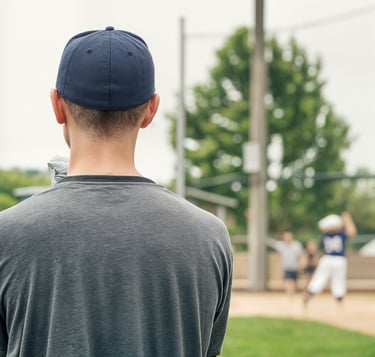 A youth baseball coach watches a game from the dugout.
