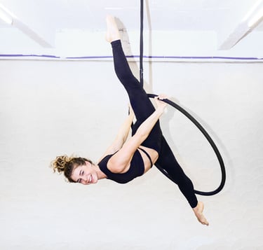 Vrouw in zwarte outfit voert een aerial hoop oefening uit bij De Polecats Fabriek in Gent