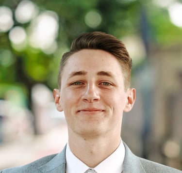 Portrait of Parker Oelrich, smiling slightly while wearing a light gray suit jacket, white shirt, an