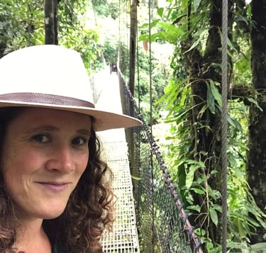 une femme aux cheveux frisés sur un pont suspendu au costa rica, un léger sourire sur les lèvres