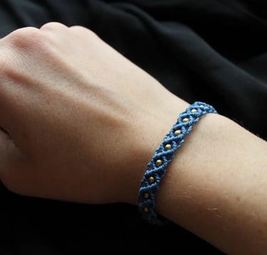 Eine Hand trägt ein dunkelblaues geknüpftes Makramee Armband mit goldenen Perlen