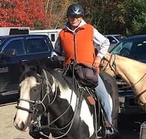 a woman in a vest and hat riding a horse