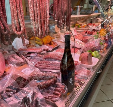 Display case at an Italian deli featuring hanging salami, vacuum-sealed cured meats, and fresh butcher cuts.