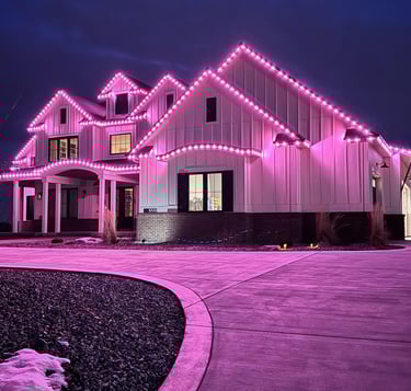 Modern white farmhouse decorated with vibrant pink LED holiday roofline lighting at night.