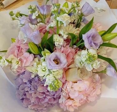 Elegant floral bouquet with pink and purple hydrangeas, lavender lisianthus, and white stocks.