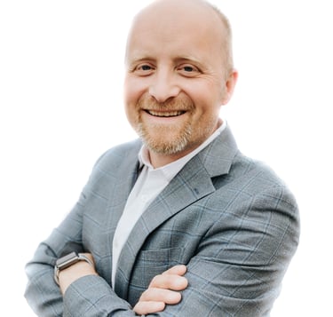 A white man with a blonde goatee. He's wearing a bright shirt and a light grey suit.