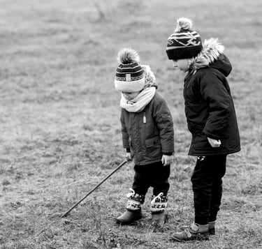 Dzieci bawią się na trawie. Chłopiec trzyma w ręku długi kijek, która imituje białą laskę.