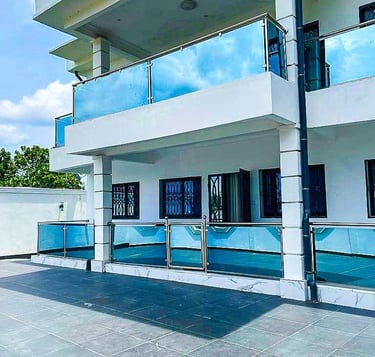 Villa de luxe moderne à Yaoundé avec façade blanche et balcons en verre teinté bleu.