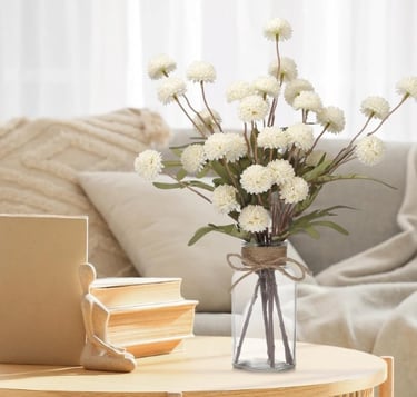 Faux white pom-pom flower stems in a glass jar vase wrapped with a burlap twine bow.