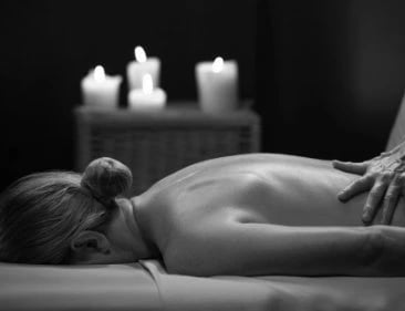 Woman lying on her front enjoying a massage, there are candles glowing in the background