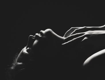 Woman lying down with her hands up by her neck.