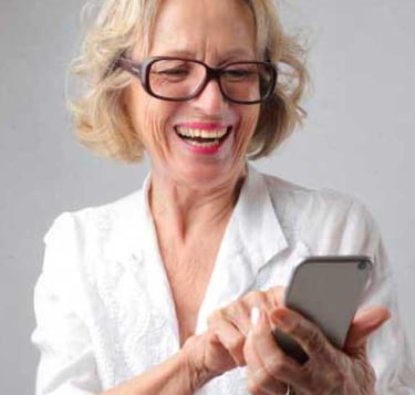 mujer mayor con gafas sonriendo mirando su smartphone