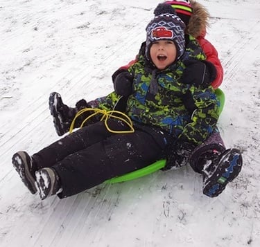 Two children sledding down a snowy hill, bundled up in winter gear, laughing joyfully.