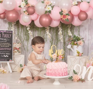a baby girl in a pink dress and a pink cake