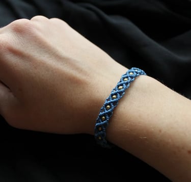 Eine Hand trägt ein dunkelblaues geknüpftes Makramee Armband mit goldenen Perlen