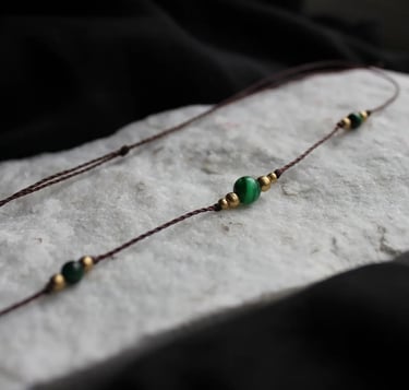 eine filigrane Kette mit grünen und goldenen Perlen liegt auf einem Stein