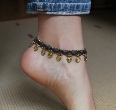 ein Fuß, welcher ein Band mit vielen goldenen Anhängern trägt