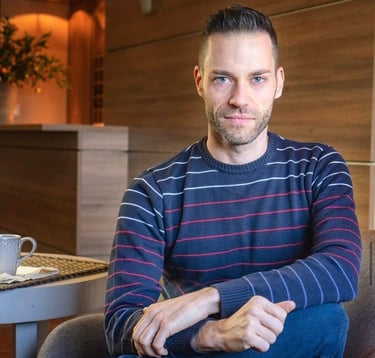 Uma foto do proprietário da empresa: homem jovem, com barba, olhos azuis, vestindo malha azul.