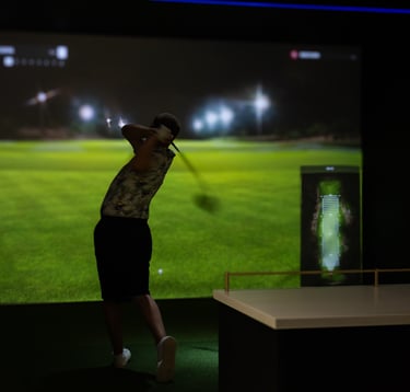 A golfer hitting a shot in a premium indoor golf simulator bay at 1IRON indoor golf