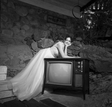 Novia divertida usando un vestido de tul y encaje, recargada en una televisión antigua