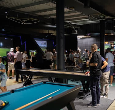 A busy event at 1IRON indoor golf simulator venue with people playing pool, shuffleboard and golf