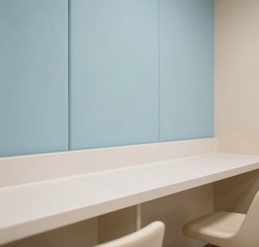 Architectural detail shot of eco-friendly materials and hygienic surfaces in a premium corporate lactation room in Hispanic / Corporate Latin America & Spain. Features soft pastel light blue sound-absorbing wall panels, smooth non-porous countertops, and subtle warm soft beige finishes. Clean professional interior photography.