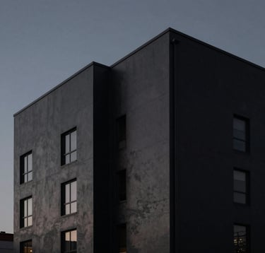 Architecture-focused shot of a matte black urban building against a dark grey twilight sky. Minimalist lighting, sharp industrial lines, and deep shadows. North American / International setting.