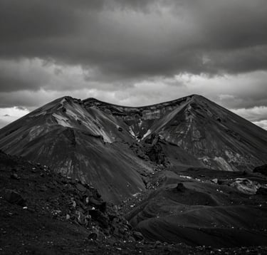 High-contrast black and white photography of a volcanic mountain ridge under a heavy charcoal sky. The composition emphasizes architectural symmetry in nature. North American / International setting.