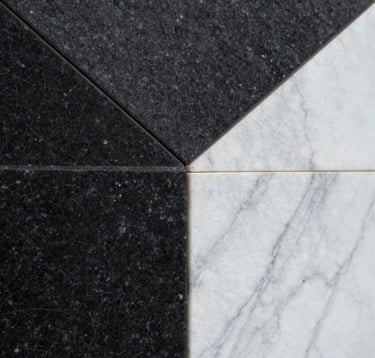 Close-up architectural detail of textured black basalt stone and sleek white marble. The composition is geometric and abstract, emphasizing light and shadow. Soft, diffused lighting. North American / International editorial style.