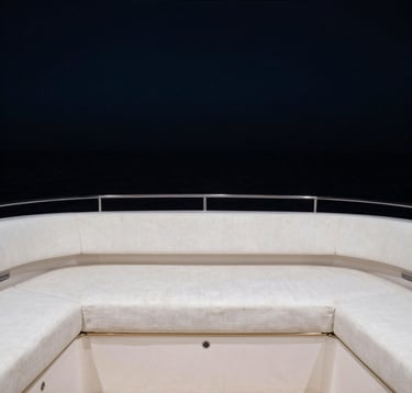 Luxury yacht interior looking out to a dark sea. Deep blacks, white linen accents, and subtle gold metal trim on the minimalist furniture. High-end editorial photography style. North American / International setting.