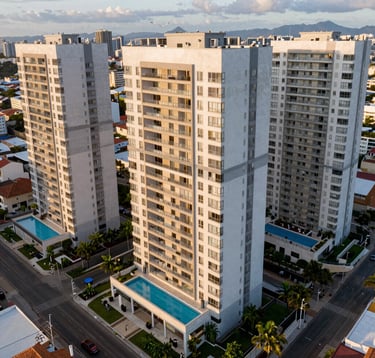 Aerial view of a luxury residential condominium in Cotia, Brazil, showing high-end houses with swimming pools and modern landscaping. Light grey and white tones dominate the architecture. Soft afternoon sun.