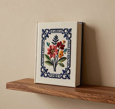 A refined architectural shot of an embroidered book displayed as a sculpture on a floating wooden shelf. The background is a clean, warm beige wall in a contemporary North American / US home. The lighting is soft and ambient, emphasizing the editorial sophistication of the piece.