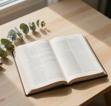 A top-down view of an open Bible resting on a clean, light-wood table next to a sprig of fresh eucalyptus. Sunlight streams in from a window, creating soft shadows. Colors include #F7FCFA and natural greens #8DAF9E. Minimalist and spiritual.