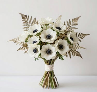 Minimalist photography of a bespoke bridal bouquet featuring white anemones and dried bleached ferns. The background is a clean, off-white studio setting. Elegant North American / US editorial style with soft shadows.