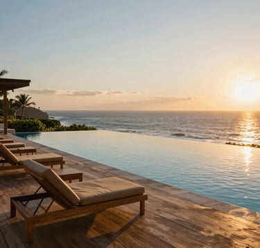 A professional photography of a luxury infinity pool overlooking the Pacific Ocean in Puerto Escondido. The setting features premium wooden decking, minimalist lounge chairs in tan tones, and clear sunset skies. The vibe is exclusive and tranquil, reflecting a high-end lifestyle.