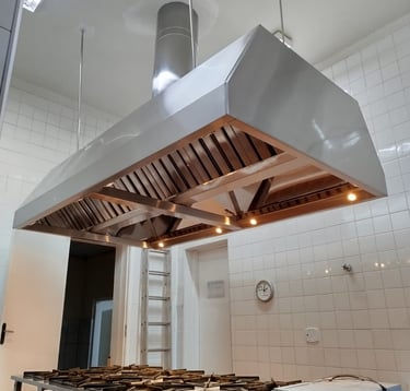 Coifa em inox sob medida instalada sobre fogão em cozinha profissional