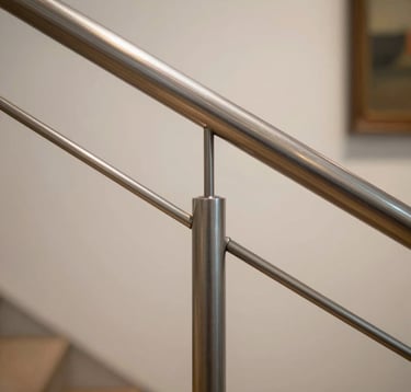 Close-up of a stainless steel handrail in a modern Brazilian art gallery. The focus is on the seamless joints and the elegant champagne-tinted reflections of the high-end interior lighting.