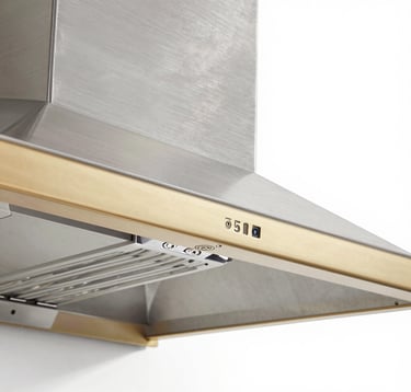 Architectural photography of a technical detail: the corner of a custom range hood where brushed stainless steel meets a champagne gold trim. The focus is on the seamless welding and the precision of the industrial finish, shot in a bright, modern studio setting.