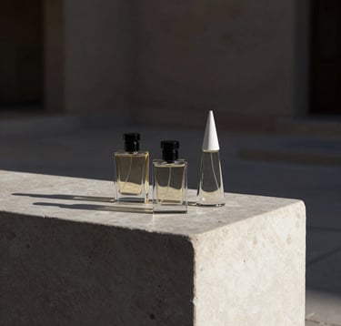 A minimalist composition featuring three architectural perfume bottles on a bone white stone plinth. Dark obsidian black shadows create a sharp, geometric feel. The setting suggests a luxury Middle Eastern / Gulf courtyard at dusk.