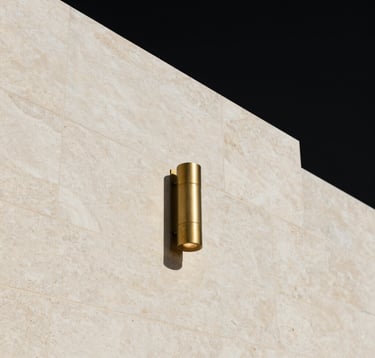 A minimalist architectural detail of a high-end luxury building in the Middle Eastern / Gulf region. Bone white stone walls meet an obsidian black sky. The composition is structured and precise, with a single muted brass light fixture casting a warm, controlled glow.