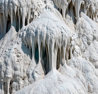 Macro photography of the calcium carbonate formations at Hierve el Agua, Oaxaca, Mexico. The textures of the white petrified 'water' drip down the cliffside like stalactites. Deep teal shadows accentuate the intricate mineral layers under bright, natural daylight.